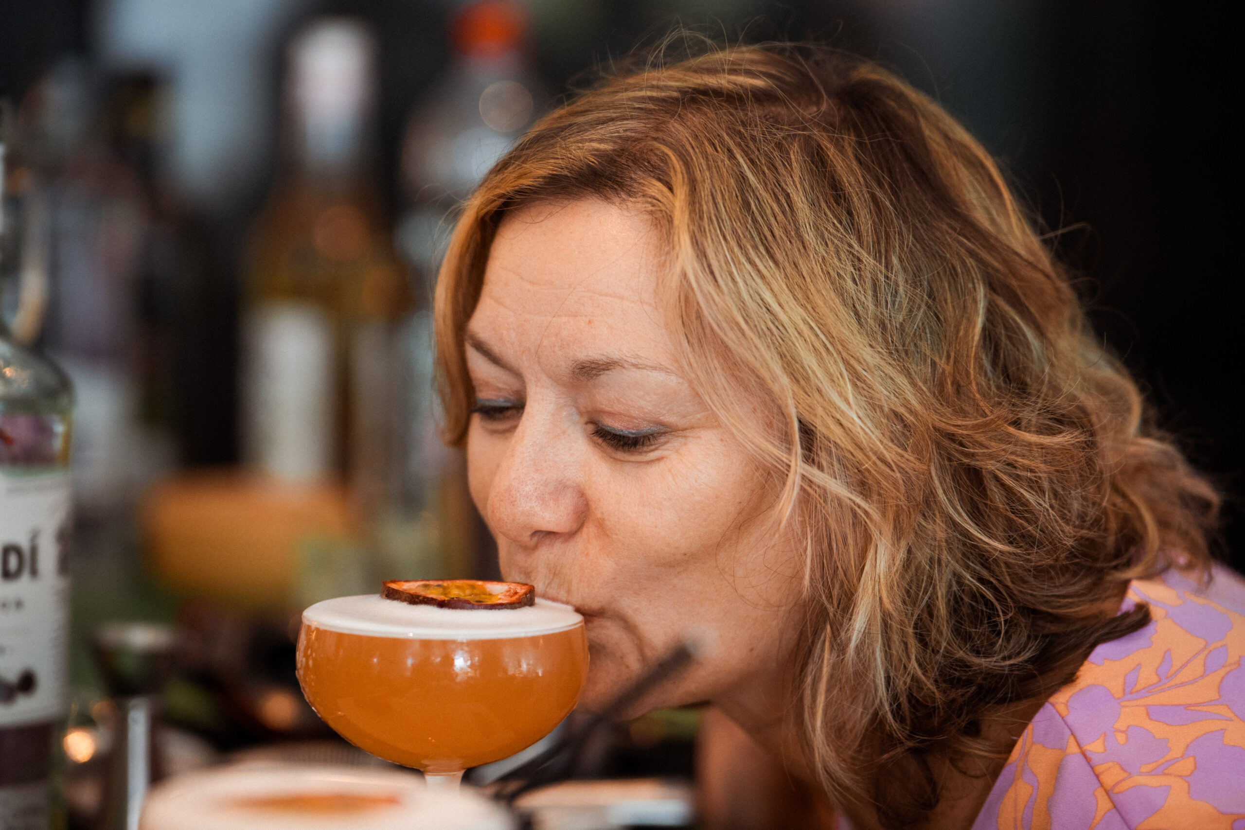 Gast neemt een slok van een oranje cocktail met een schijf passievrucht op het schuim