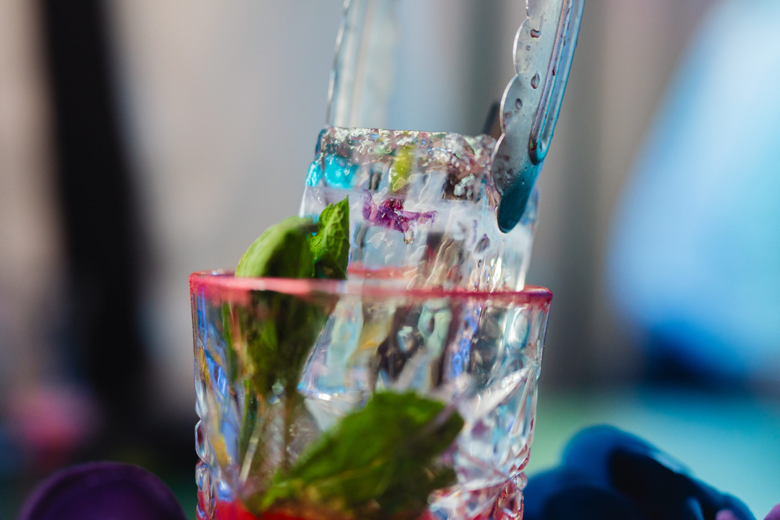 The bartender uses tongs to lower a large block of ice containing a frozen flower into a cocktail glass