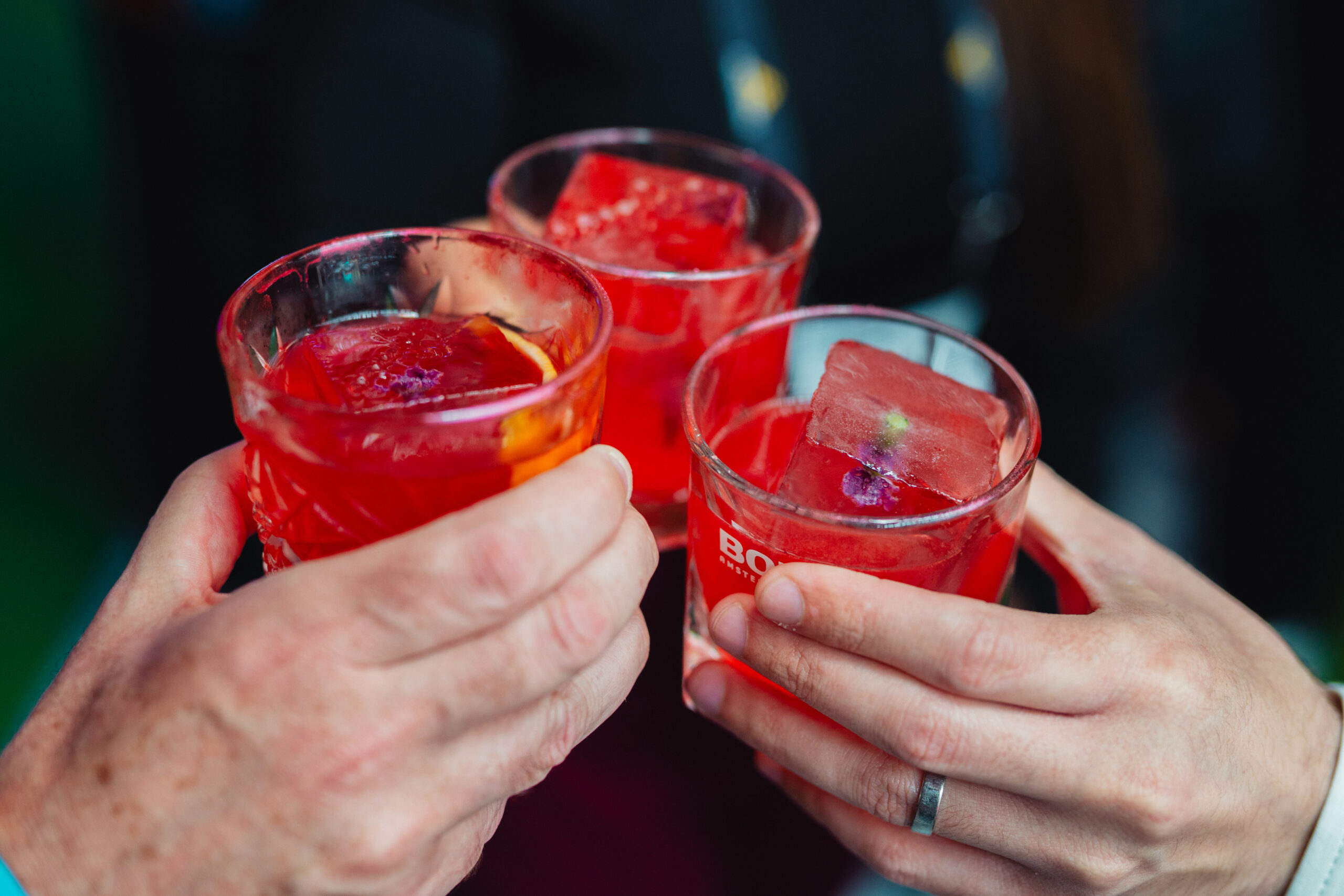 Drie gasten proosten met rode cocktails met ijsblokken waarin bloemen zijn ingevroren
