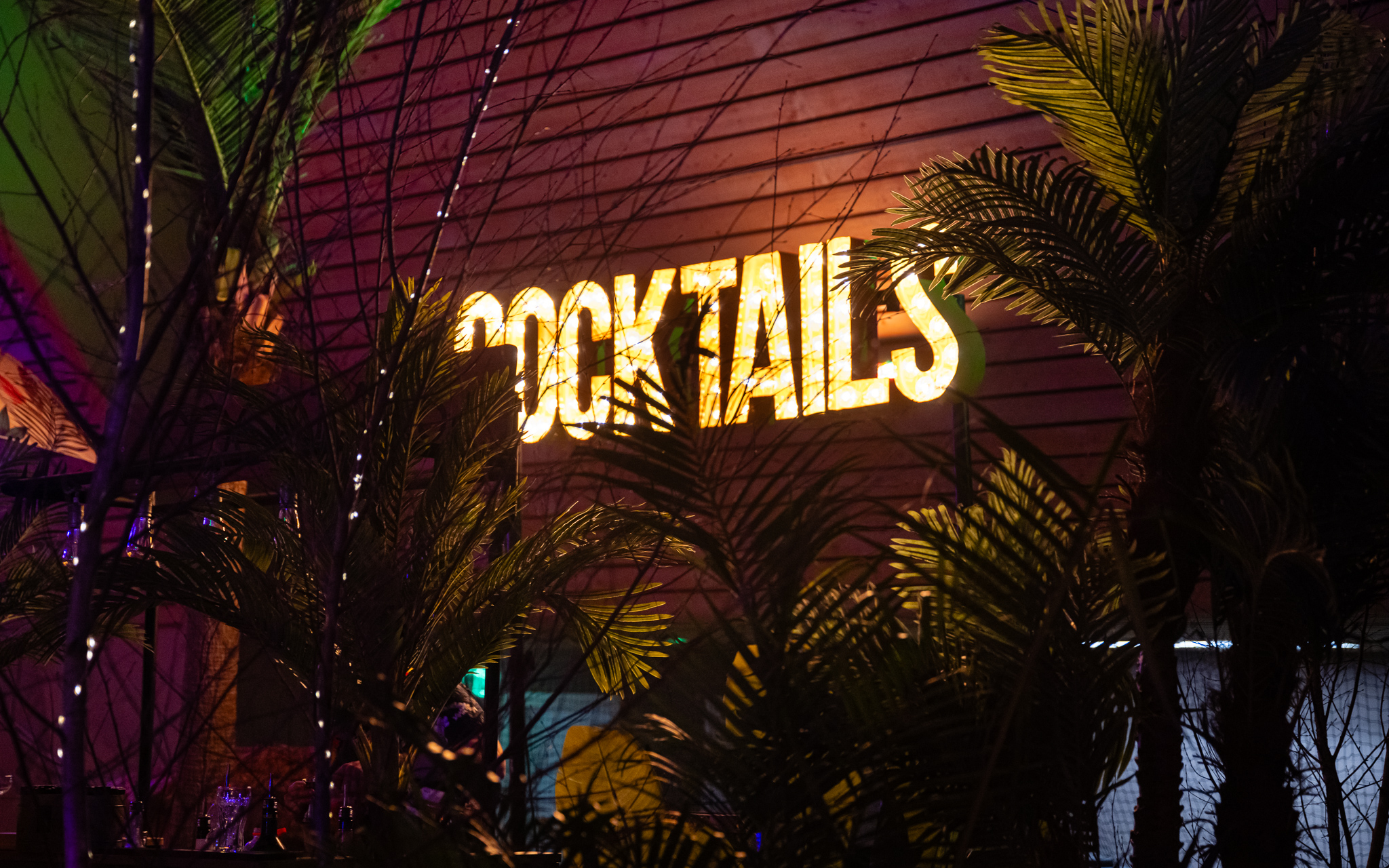 Verlichte cocktailletters tussen palmbladeren op een avondfeest