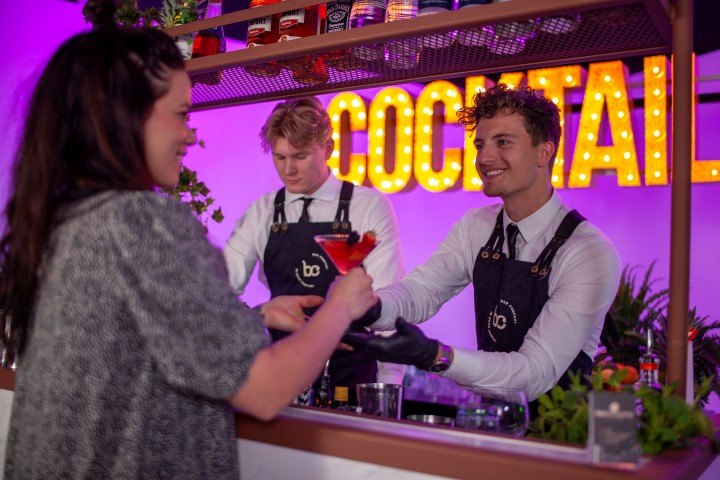 Twee jonge bartenders van Bar Company serveren cocktails aan een gast