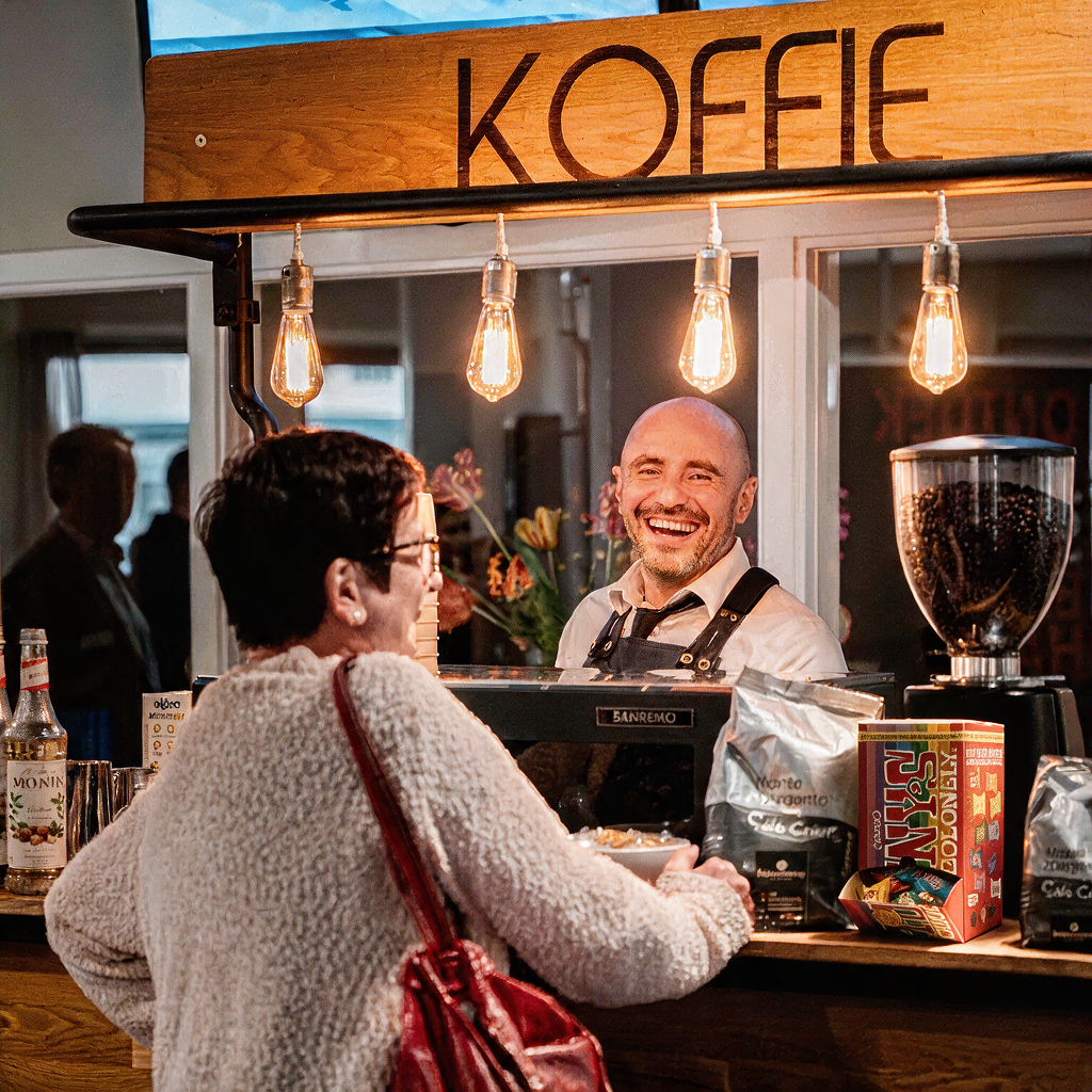 Lachende barista achter de koffiebar van Bar Company, met Tony's Chocolonely naast de koffiebonen